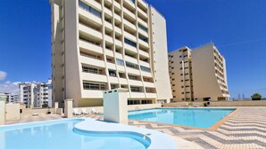 Ett poolområde med en böjd pool och solstolar, omgivet av flervåningsbyggnader med balkonger.