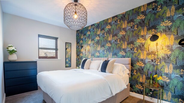 Ein Schlafzimmer mit einem Bett, einem Schminktisch, einem Fenster und einer Wand mit Blumenmuster.