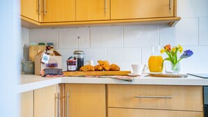 Eine Küche mit Holzausstattung, einer Kaffeemaschine, Croissants, einer Obstschale und einer Vase mit Blumen.