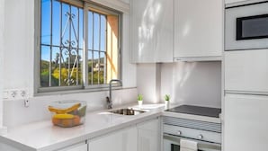 Una cocina moderna con armarios blancos, un lavamanos de acero inoxidable y una ventana con rejas decorativas de hierro.