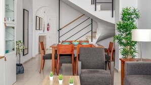 Una sala de estar moderna con comedor, que incluye una escalera, una planta en maceta y una lámpara.