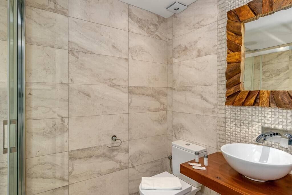 A bathroom with marble tiles, a wooden vanity, a white sink, and a toilet.