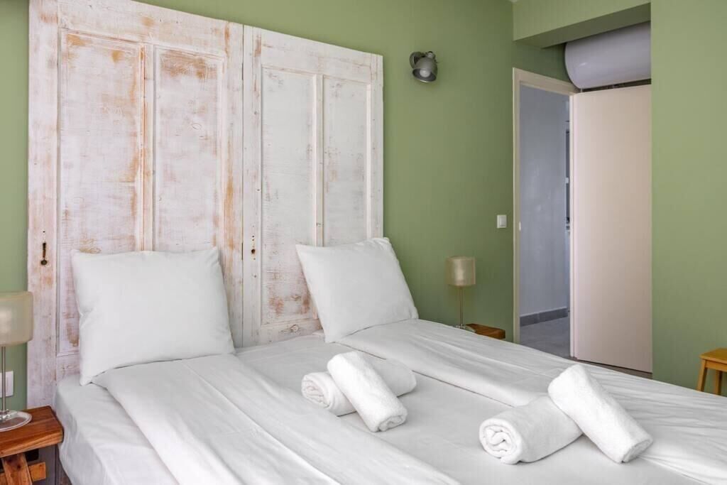 A room with a bed, two pillows, a nightstand, a lamp, and a door.