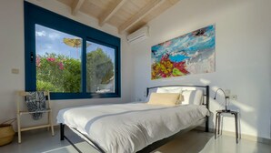 A modern bedroom with a large bed, a painting, and a view of greenery outside. - Villa Saphora in Lefkada (Lefkada)
