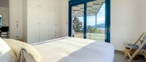 A bedroom with a large bed, a wardrobe, and a view of the outdoors through a glass door.