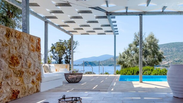 A modern outdoor seating area with a stone wall, a white sofa, a woven basket, and a view of the sea. - Villa Saphora in Lefkada (Lefkada)