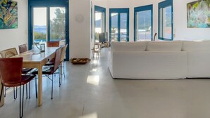 A spacious living area with a white sofa, dining table with chairs, and large windows offering a view of the outdoors. - Villa Saphora in Lefkada (Lefkada)