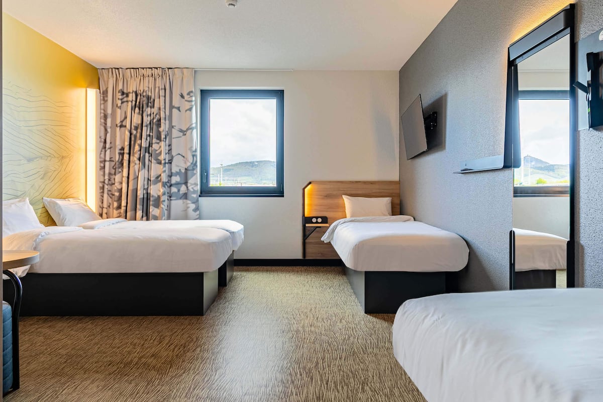 Ein Hotelzimmer mit zwei Betten, einem großen Fenster, einem Flachbildfernseher und einem kleinen Tisch mit einer Lampe.