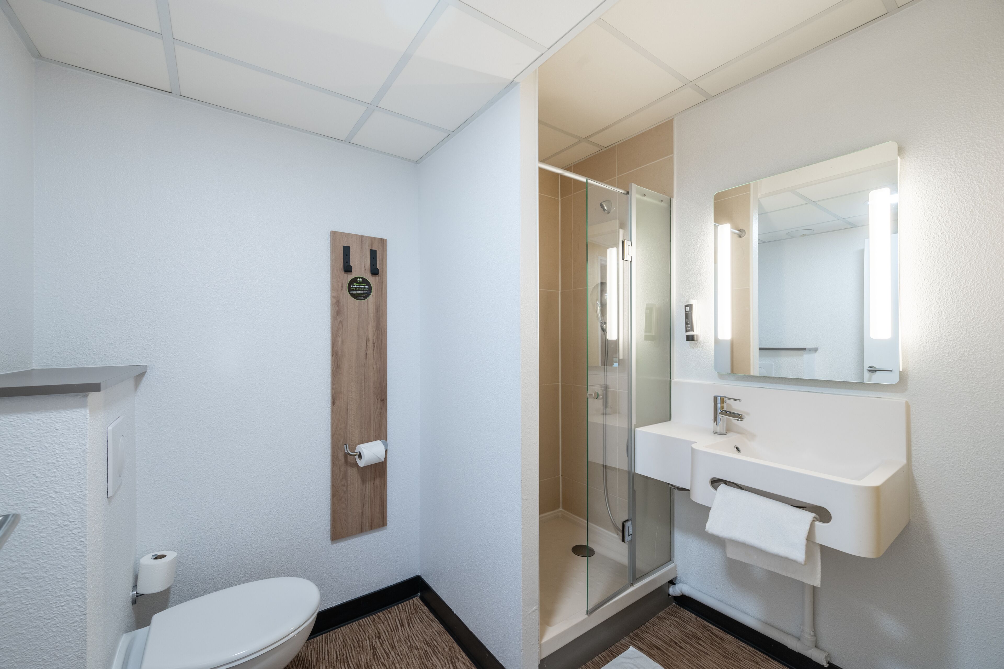 Une salle de bain moderne comprenant des toilettes, une douche à parois de verre, un lavabo avec un miroir et une porte en bois.