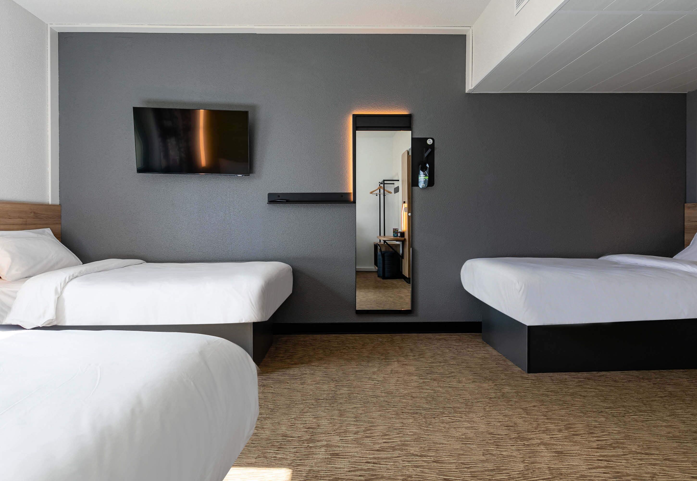 Une chambre d’hôtel avec deux lits, un téléviseur à écran plat fixé au mur et un miroir avec un bandeau lumineux.
