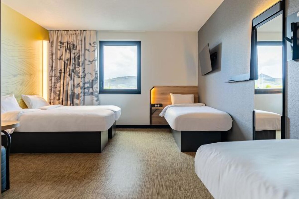 Een hotelkamer met twee bedden, een groot raam, een flatscreentelevisie en een spiegel.