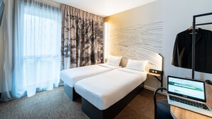 Een hotelkamer met twee bedden, een laptop op een bureau en een groot abstract kunstwerk aan de muur.