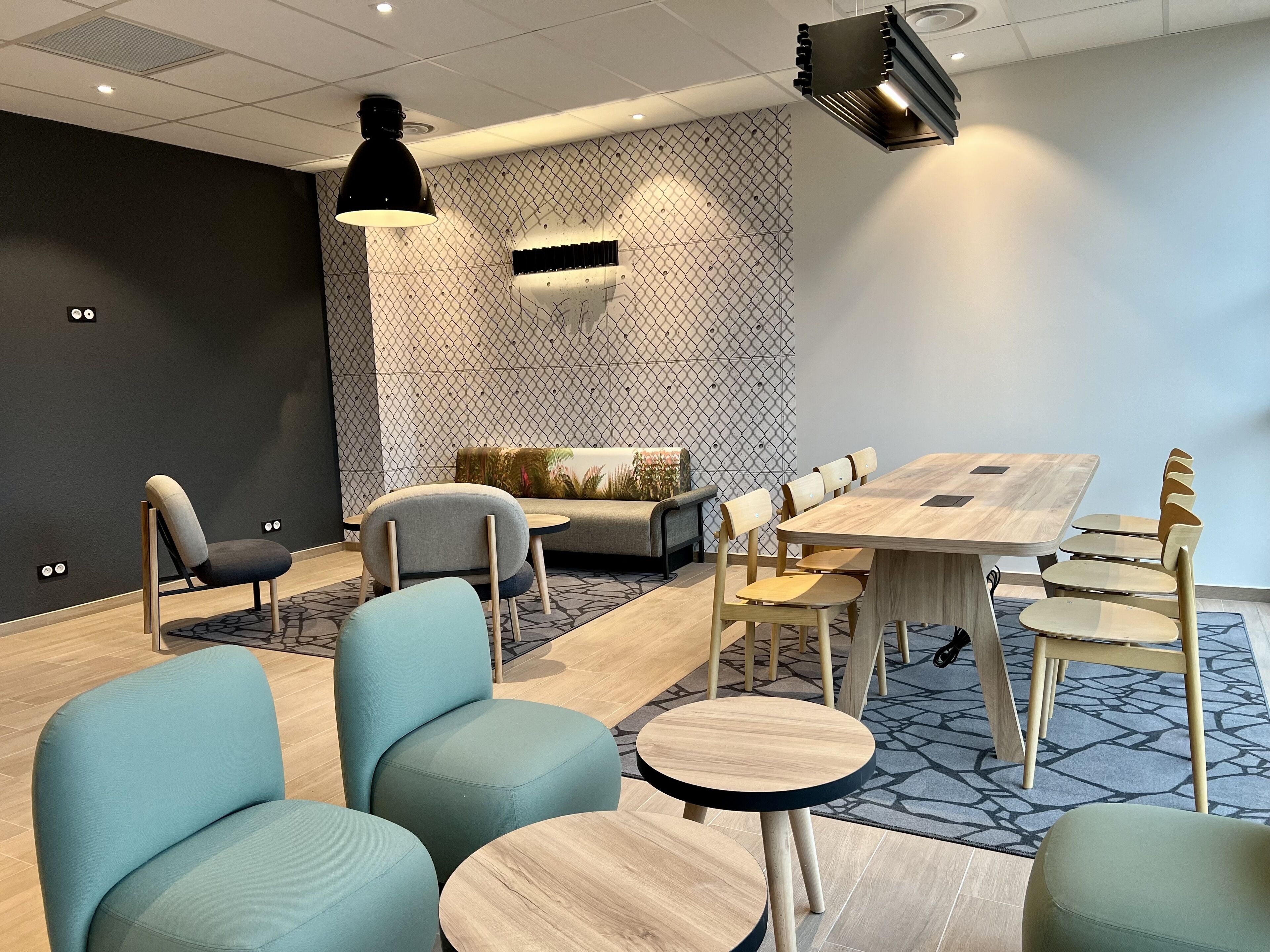 A modern meeting room with a large wooden table, several chairs, a sofa, and a patterned wall.