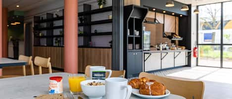 A breakfast setting with a table, breakfast items, and a view of the kitchen area.
