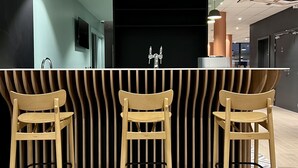 Een moderne bar met drie houten barstoelen, een zwart-wit gestreepte toonbank en hanglampen.