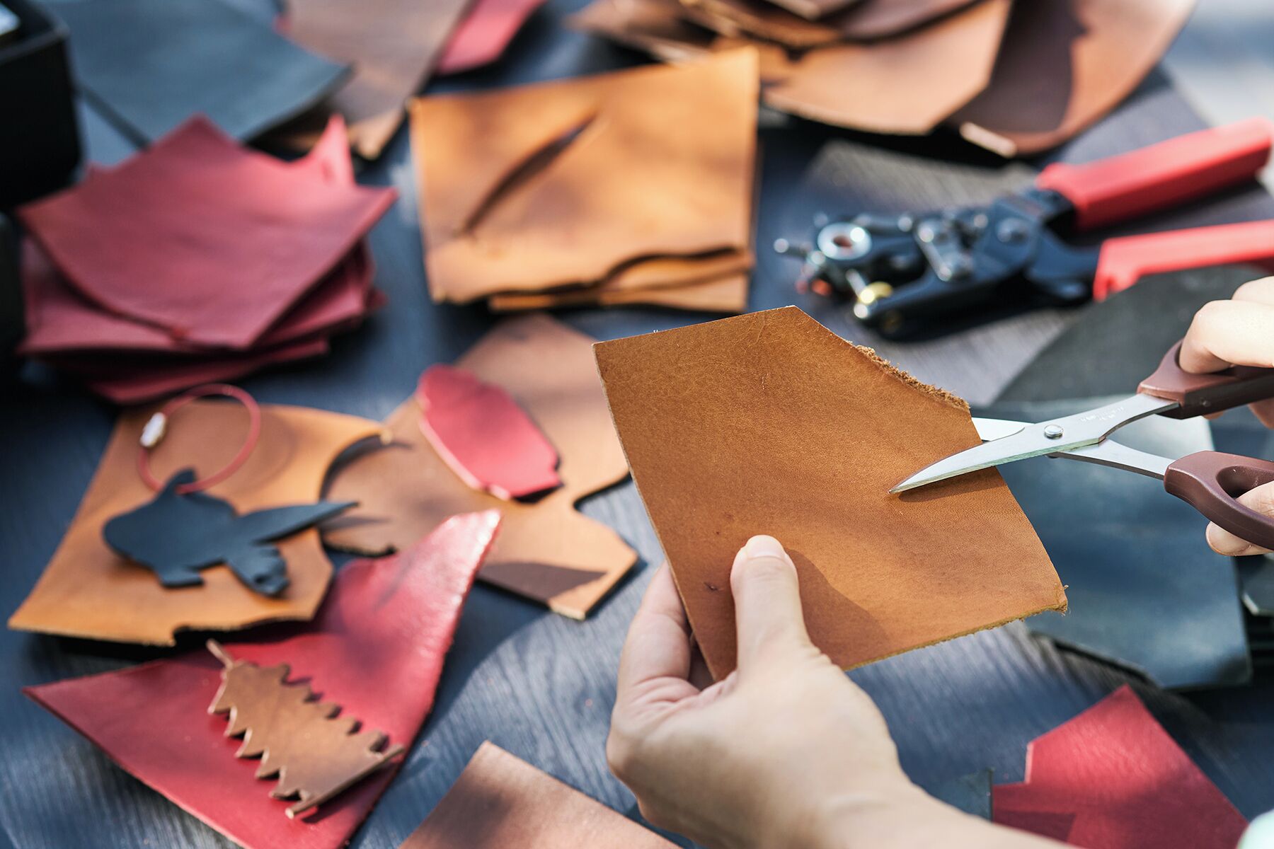 Hands cutting a piece of brown leather.