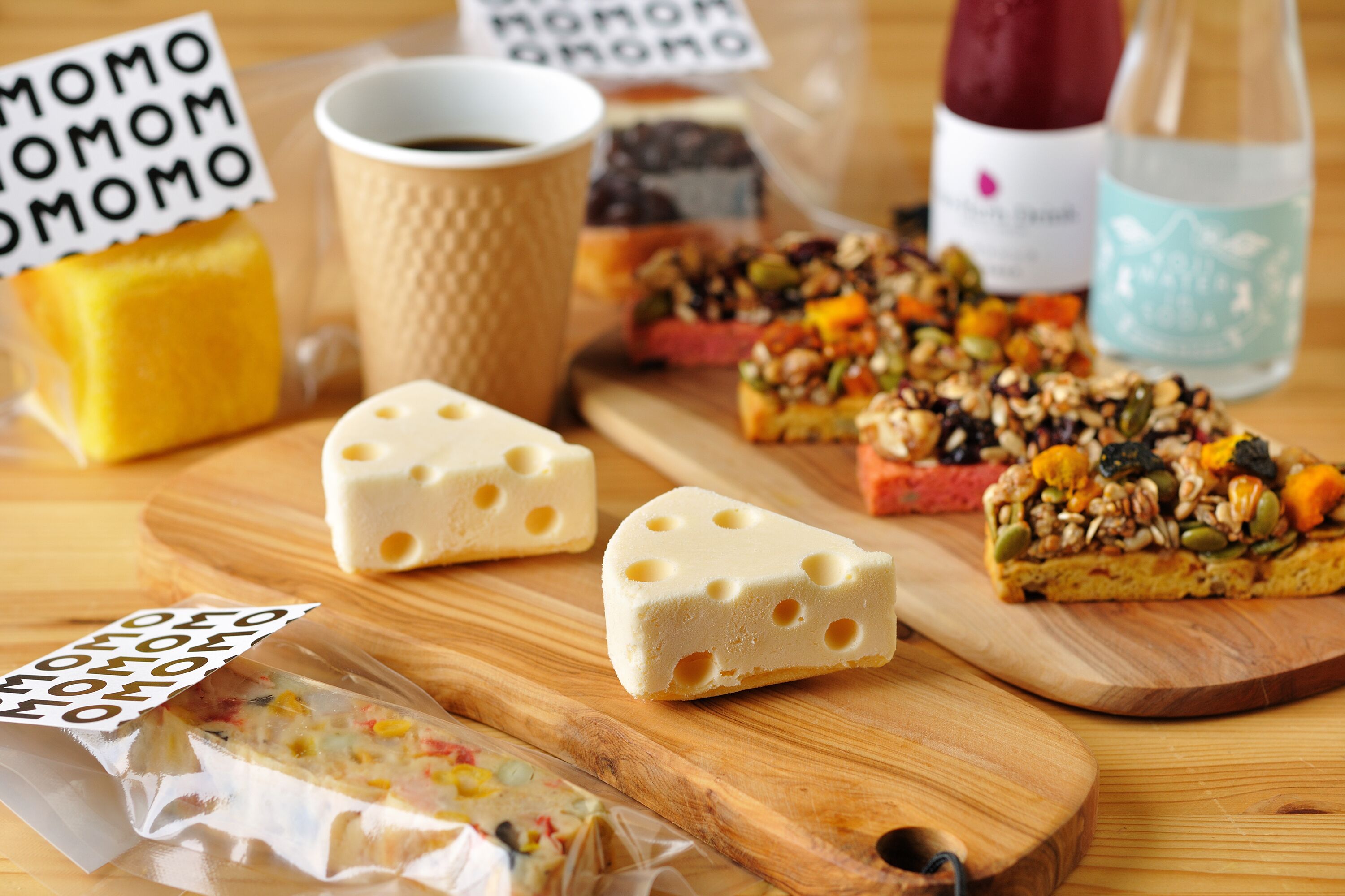 Une table en bois sur laquelle se trouvent divers aliments, notamment du fromage, une tasse de café et une bouteille d’eau.
