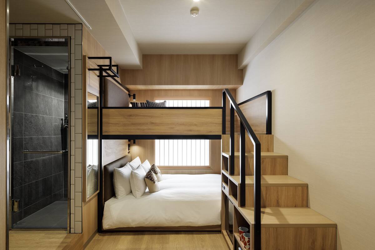 A modern bedroom with a bunk bed, wooden flooring, and a staircase.