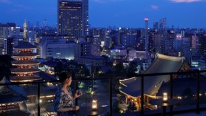 A woman standing by a balcony overlooking a traditional Japanese temple with a cityscape in the background. - OMO3 Asakusa by Hoshino Resorts (Tokyo)