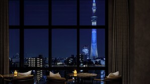 A room with a large window offering a nighttime cityscape view, including a prominent tower. There are two chairs and a small table with a candle. - OMO3 Asakusa by Hoshino Resorts (Tokyo)