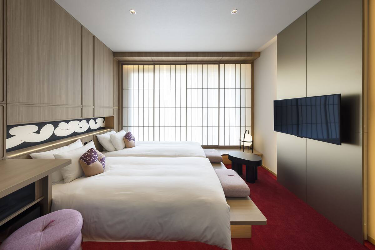 A modern hotel room with two beds, a TV, a desk, and a large window.