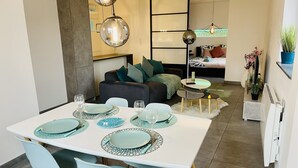 A modern dining area with a white table set for four, light blue chairs, and a contemporary chandelier. - Sublime atypical apartment Le Puits (Noisseville)