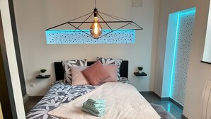 A modern bedroom with a geometric ceiling light, a patterned bedspread, and a neatly folded towel on the bed. - Sublime atypical apartment Le Puits (Noisseville)