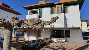 A two-story white building with a flat roof, a balcony on the upper floor, and a small patio area with a table and chairs.