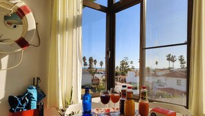 A table with fruits, beverages, and a box of instant coffee, overlooking a coastal view with palm trees and houses.