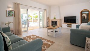 A living room with a sofa, TV, fireplace, and a view of the outdoor patio. - Vivenda Pomba Beautifully renovated with heated pool! (Carvoeiro)
