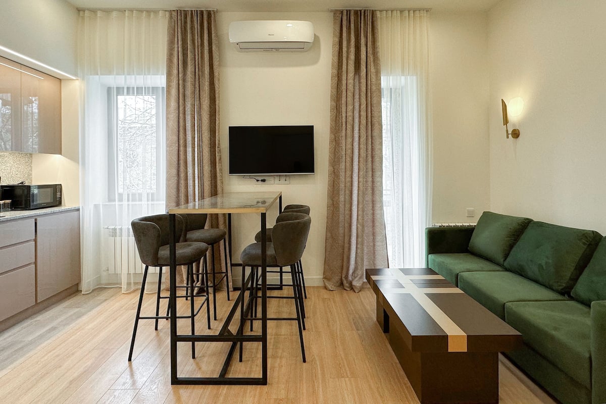 Un salon moderne avec un canapé vert, une table basse, un téléviseur et un coin repas comprenant des chaises et une table.