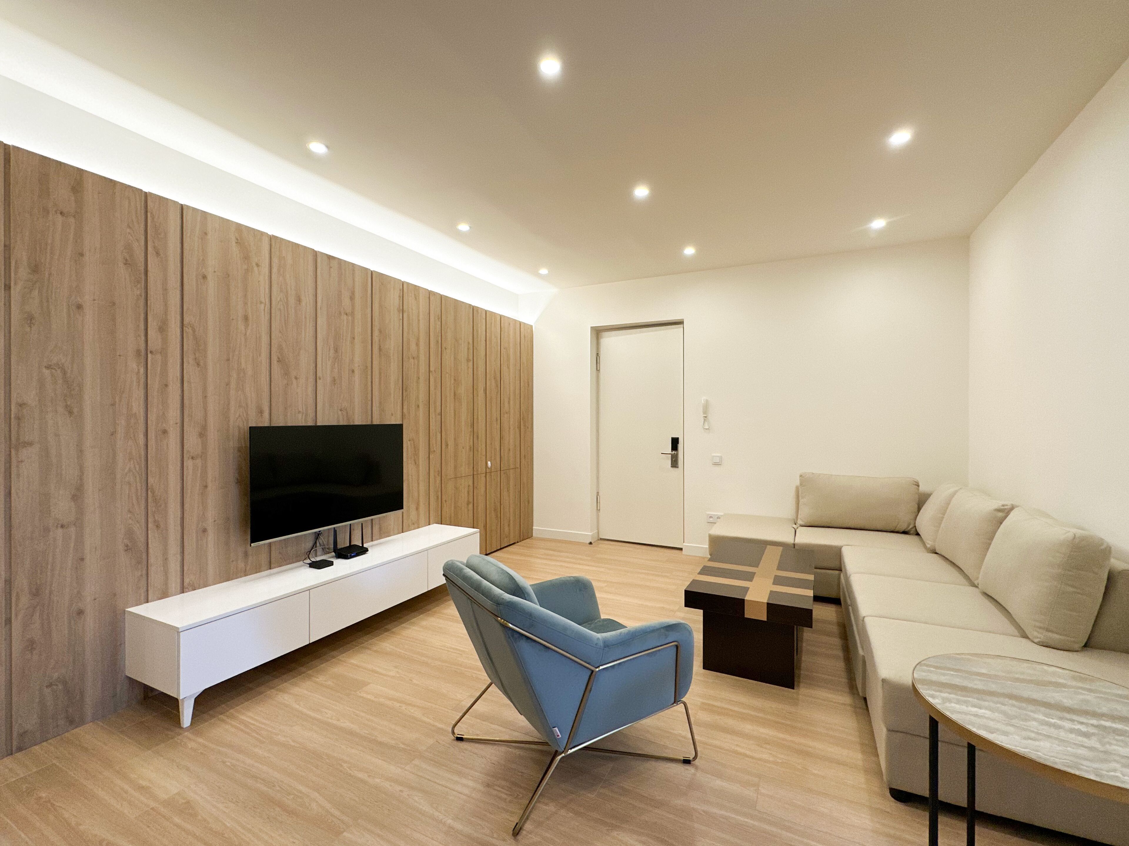 Un salon moderne avec un téléviseur à écran plat, un fauteuil bleu, un canapé et une table basse.