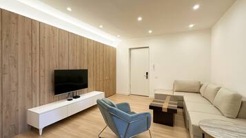 A modern living room with a flat-screen TV, a blue chair, a sofa, and a coffee table.