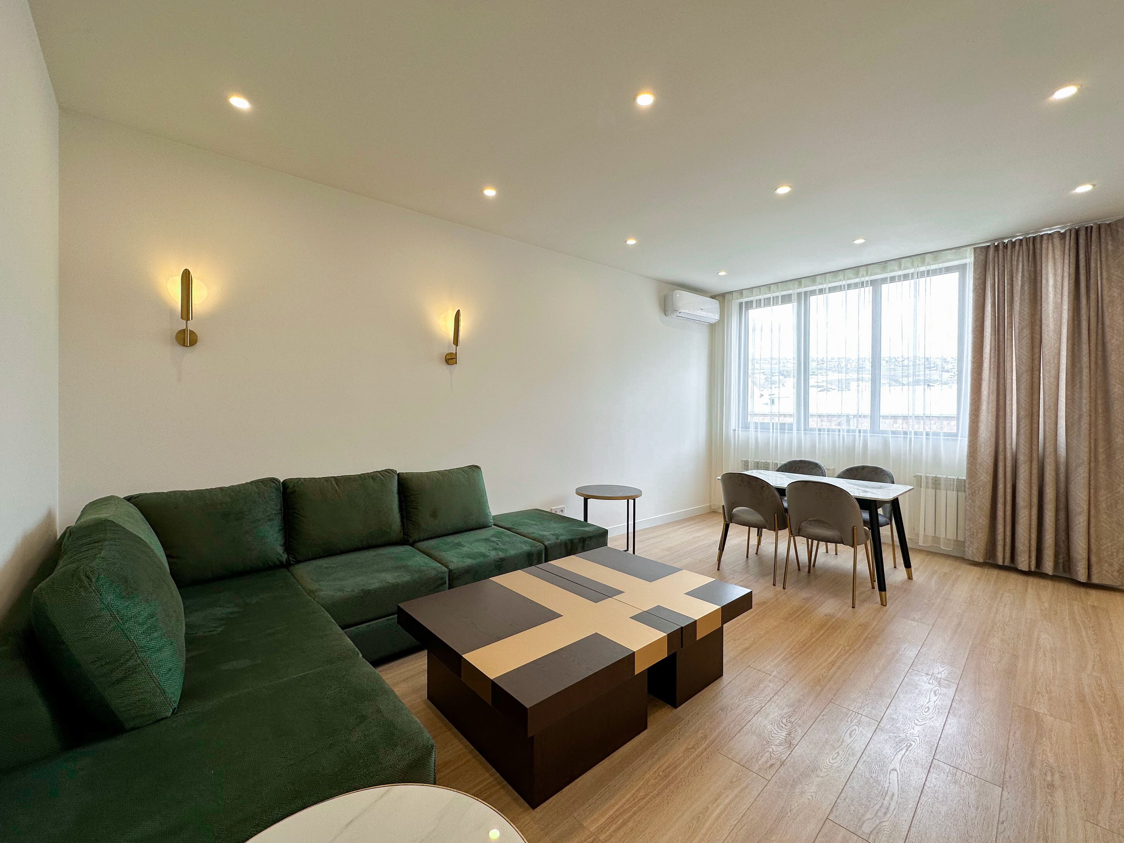 A modern living room with a green sofa, a wooden coffee table, and a dining area with chairs and a table.