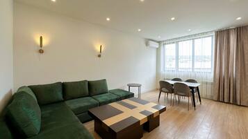 A modern living room with a green sofa, a wooden coffee table, and a dining area with chairs and a table.