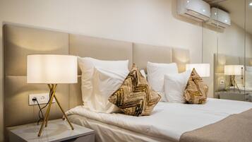 Una habitación de hotel con una cama grande, ropa de cama blanca y almohadas decorativas. Hay una mesita de noche con una lámpara y un enchufe.