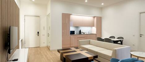 A modern living room with a sofa, coffee table, and blue armchair. A kitchen is visible in the background with cabinets and a countertop.