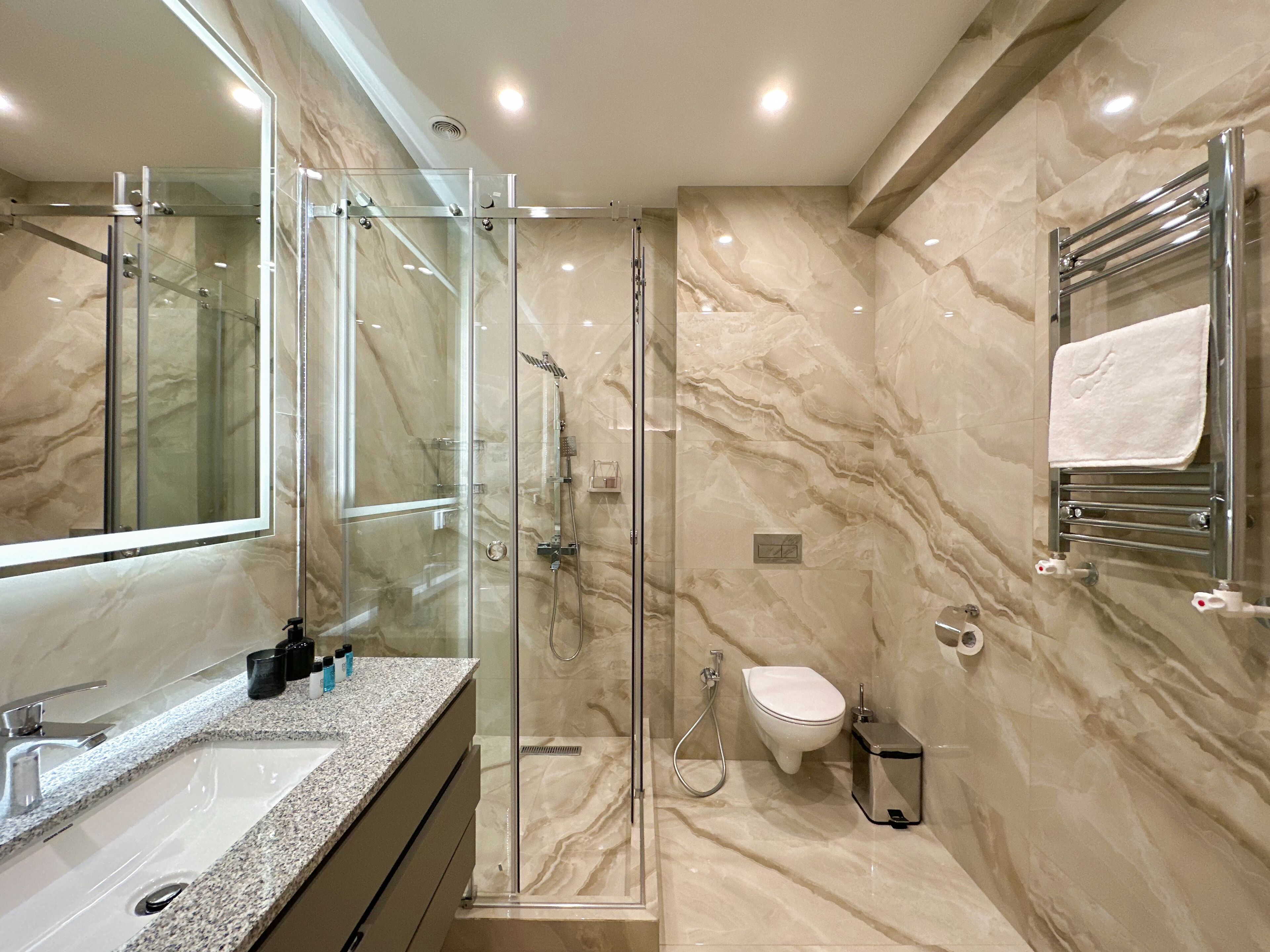 A modern bathroom with a glass-enclosed shower, a large mirror, a sink, and a toilet.