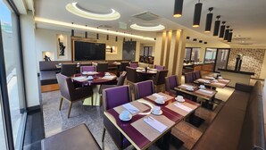 Un restaurante moderno con mesas redondas, sillas moradas y una amplia pantalla de televisión.
