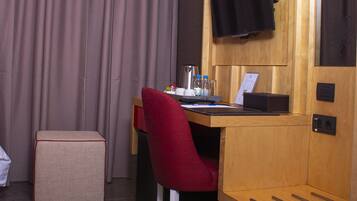 Une chambre d’hôtel avec un bureau en bois, une chaise rouge, un téléviseur fixé au mur et une grande fenêtre avec des rideaux.