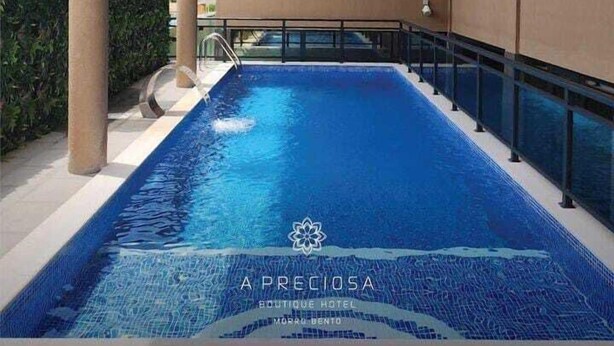 Una piscina con superficie de agua azul cristalina, rodeada por un edificio moderno con grandes ventanales y fachada color beige.