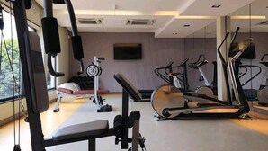 Un gimnasio moderno con diversos equipos de ejercicio, un espejo grande y una televisión en la pared.