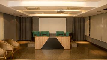Un salón de conferencias con una pantalla grande, dos sillas verdes y un atril.