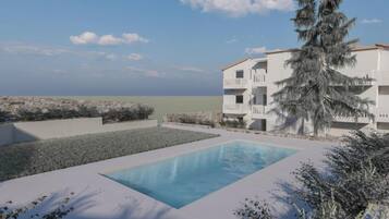 A swimming pool with a view of the sea, surrounded by a white building with balconies, and a tall pine tree.