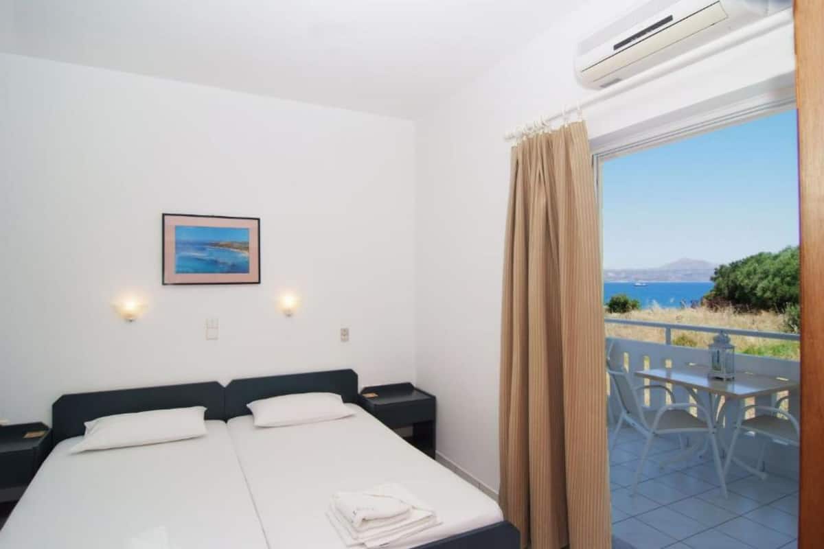Une chambre d’hôtel avec un lit, des tables de chevet, un tableau au mur et une vue sur la mer par la fenêtre.