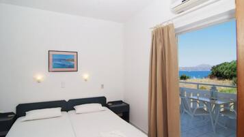 Una habitación de hotel con cama, mesitas de noche, un cuadro en la pared y vista al mar a través de una ventana.