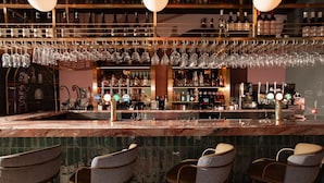 A bar area with multiple shelves of bottles, hanging glasses, and bar stools. - The Address Glasgow (Glasgow)