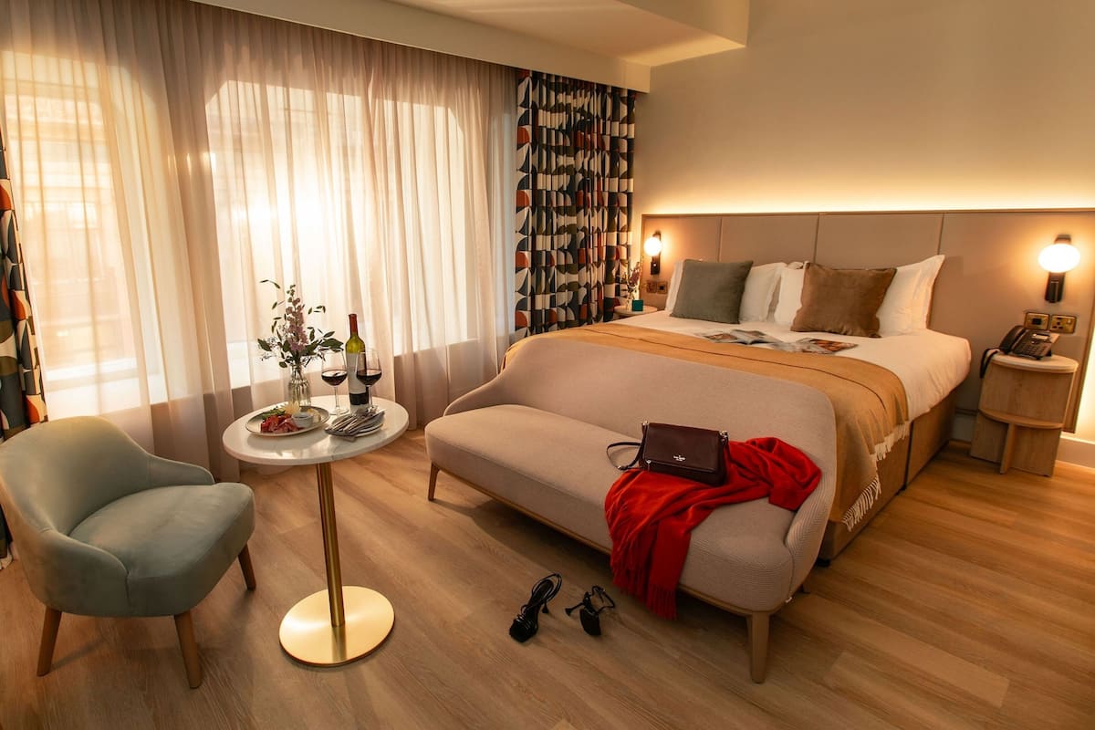 Ett modernt hotellrum med en stor säng, en sittgrupp med ett bord och ett litet sidobord med en lampa.