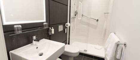 Une salle de bain moderne avec un lavabo, des toilettes et une douche, le tout de couleur blanche.