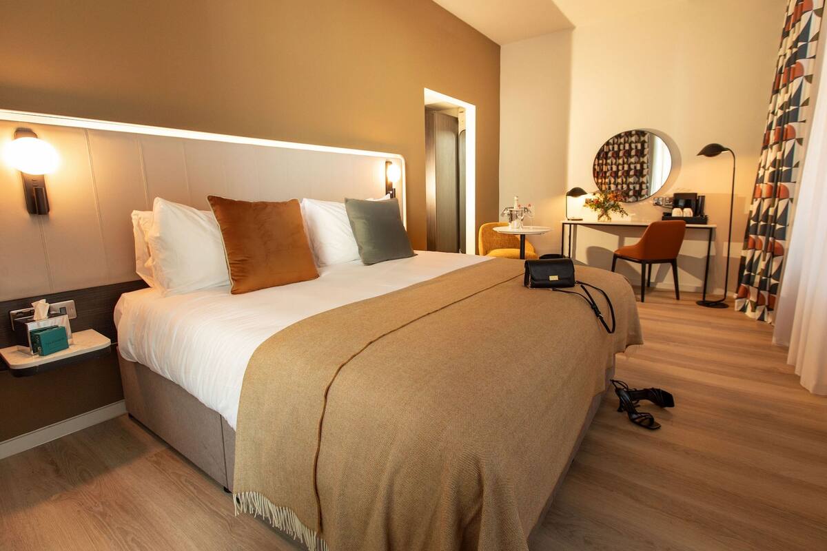 Ett modernt hotellrum med en stor säng, ett nattduksbord och ett skrivbord med en stol.